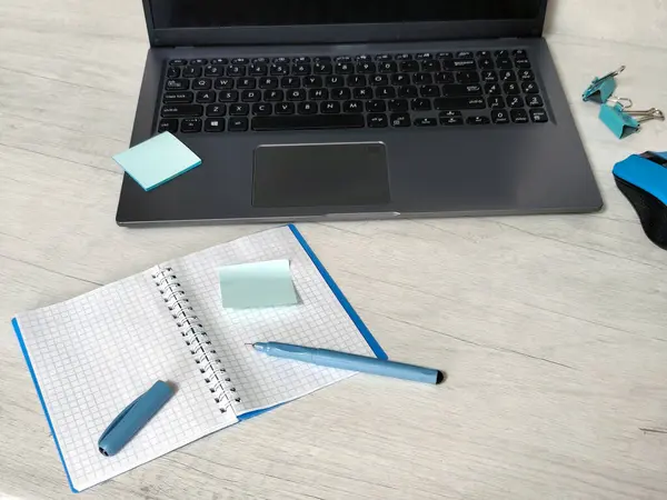 Laptoplu iş yeri, mavi kablosuz fare, zarflar, defter, ofis masası, ahşap masadaki yapışkan notlar. İş, planlama, uzaktan çalışma konsepti, serbest çalışma, not defterine yazma süreci eğitimi