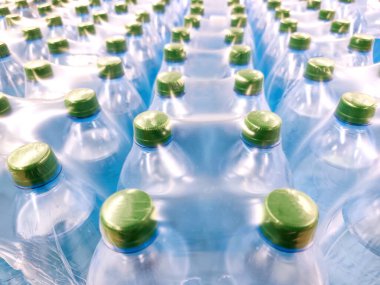 Çoklu plastik su şişeleri sıkıca paketlenmiş, yukarıdan görülüyor. Yeşil başlıklar, mavi tonlu şişeler, temiz, taze görsel, hidrasyon, seri üretim, şişe su endüstrisi, ambalaj ve lojistik.
