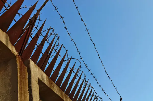 Paslı çiviler ve dikenli teller açık mavi gökyüzüne karşı. Kısıtlamanın, korumanın ve güvenliğin sembolü. Hapishane, kapalı bölge