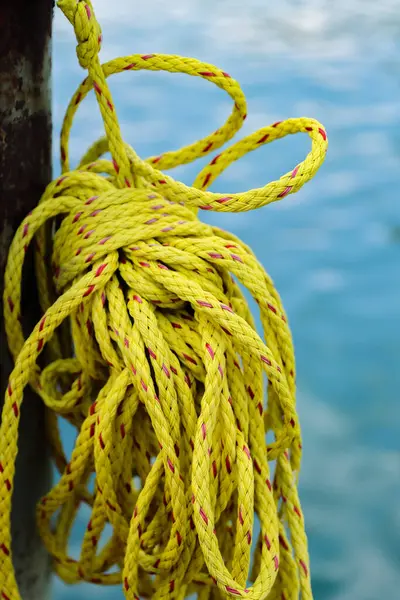 Limandaki ahşap korkulukta asılı sarı yelkenli halat bobini. Bulanık arka planda mavi deniz suyu. - Yakın çekim. Seçici odak