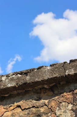 Çatlak, beton yamalı, arka planda beyaz bulutlu mavi gökyüzü olan eski gri kahverengi taş duvar. Düşük açı. Kontrast tasarım konsepti. Karanlık ve aydınlık. Boşluğu kopyala