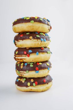 Çikolata ve renkli ukalalarla kaplı bir yığın çörek. Beyaz arka planda 5 çörek yığını var. Yan görüş. Boşluğu kopyala