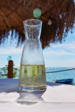 Deniz kıyısındaki restoranın masasındaki cam sürahide taze meyve suyu. Sahilde buz gibi limonata. Şişenin ayrıntıları. Bir damla su. Arka planda mavi gökyüzü ve deniz. Yakın plan.