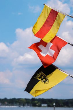 Rüzgarda dalgalanan bayrak direğinde üç bayrak. Baden, İsviçre bayrakları, amblemli Bayrak Baden-Wrttemberg. İsviçre bayrağı ortada. Mavi gökyüzünde ve beyaz bulutlarda izole. Boşluğu kopyala.