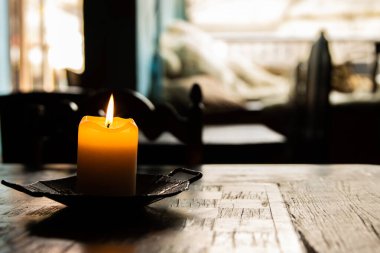 Kafe satranç tahtasındaki ahşap masada yanan turuncu mum. Arka plandaki pencere bulanık. Antika metal mum tutacağı. Sıcak romantik atmosfer. Kapatın. Seçici odak