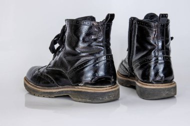 Çok yıpranmış bir çift botun ön görüntüsü. Eski, kırık siyah deri dantelli yüksek çizmeler. Moda ayak bileği çizmeleri. Şık kadınların erkek üniformaları. Ayakkabı bağcıklı Grunge botları. beyaz arkaplanda izole