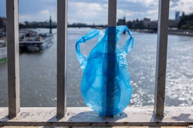 Budapeşte 'de Donau nehrinin üzerindeki Elisabeth köprüsünün korkuluklarında asılı duran mavi plastik torba. Şehirde çöp var. Çevre kirliliği kavramı. Ekolojik felaket, felaket. Seçici odak