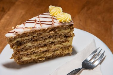 Beyaz tabak, ev yapımı lezzetli, fındık ve kremalı Esterhazy keki. Peçete ve çatalla servis edilen lezzetli Esterhazy Torte. Kafedeki ahşap masa. Seçici odak