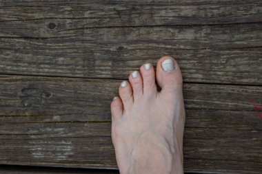 Suyun üzerinde beyaz inci ojeli yalın ayak bir kadın. Gölde dinleniyor, nehir kıyısında oturuyor. Doğada dinlenmek. Gökyüzü yansıması. Mutlu yaz günleri. Üst görünüm