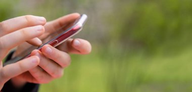 Kırmızı cep telefonunun siyah ekranında işaret parmağı. Mesaj atan kişi, hippi dokunuşlu akıllı telefon ekranı. El ele tutuşan kızlar çalışıyor. Yaz parkı. Kapatın. Uzayı kopyala Seçici odak