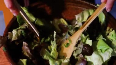 Mutfakta vejetaryen salatası yapıyorum. Evde salata hazırlarken marul, baharat ve zeytinyağını iki plastik spatulayla karıştıran tanınmamış bir kadın. Vejetaryen salatası. Üst görünüm