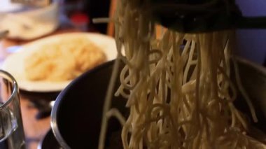 Annem tencerede ya da tavada sıcak spagetti ya da makarna servis ediyor ve tabağa beyaz koyuyor. Adam bulanık arka planda parmesan sürüyor. Akşamları aile yemeği.