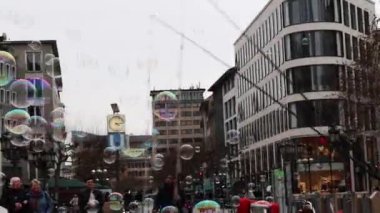 Frankfurt am Main, Hessen, Almanya. 24 Şubat 2023. Bir adamı izleyen insanlar ve çocuklar şehrin merkezinde kordon düğümlü dev renkli sabun köpükleri yapıyorlar. Çocuklar kabarcıkları yakalıyor.