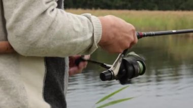 Yakın çekim ekipmanları ve tanınmayan sinek avcılarının elleri. Fisher olta makarasını döndürüyor. Yırtıcı balıkları taze suda avlarken bir adam halatta sallanıyor. Finlandiya 'da yaz