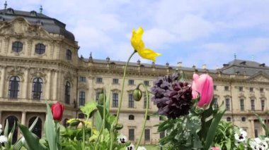 Wuerzburg Malikanesi ve bahçesinin panoramik manzarası. Birçok güzel çiçek rüzgarda titreyerek el sallıyor. Mavi gökyüzü ve bulanık arka plandaki Konut Sarayı. Mükemmel güneşli bir gün..