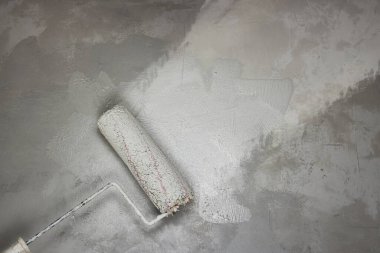 İşçi el boyası duvar yüzeyini boya silindiriyle boyuyor. Apartman yenileniyor. Fırça fırçası, aşınmadan korunmak için duvarı beyaz renge boyar. Boş kopya alanı desenli arkaplan. Kapat..