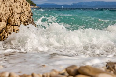 Güçlü dalgalar, kayalık bir Nugal plajında mavi gökyüzüne çarpıyor. Dalga taşlı bir kıyıya vuruyor. Manzaralı deniz manzarası. Kart, afiş, seyahat katalogu fotoğrafı. Uzayı kopyala Seçici odak.