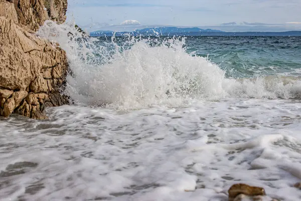 Kayalık bir sahilde güçlü dalgalar eziliyor. Dalga taşlı bir kıyıda kırılarak bir sprey oluşturur. Manzaralı deniz manzarası. Kart, afiş, seyahat katalogu fotoğrafı. Uzayı kopyala Seçici odak.