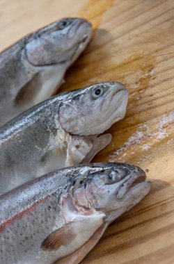 Eski tahta kesme tahtasına üç taze alabalık oyuyorum. Tatlı su gökkuşağı forel balığı pişirmek. Corhynchus 'un öpücükleriyle doğrama tabağında. Ahşap arka. Kapatın. Uzayı kopyala Üst görünüm