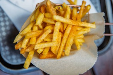 Kahverengi parşömen kağıdıyla kaplı şık bir tel sepetin içinde servis edilen kızarmış patates kızartmasının yakın görüntüsü. Yemek fotoğrafçılığı, restoran menüleri ve mutfak promosyonları için ideal. Seçici odak