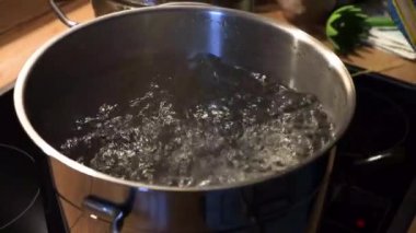 Mutfak sobasındaki kaynar suya spagetti ekleniyor. Lezzetli bir yemek için paslanmaz çelik bir tencerede ev yapımı İtalyan yemeği pişirmek. Geleneksel aşçılık, ev yemeği. 4K video