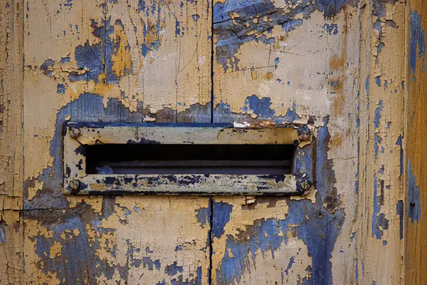 stock image Closeup image of a weathered, peeling paint on an old wooden door with a vintage mail slot, perfect for backgrounds, textures, and rustic-themed designs. Copy space