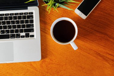 İş yerindeki ahşap masadaki sıcak Americano 'nun yanında bilgisayar defteri ve akıllı telefon var. Laptop ve cep telefonlu sıcak kahve..