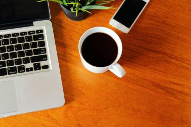 İş yerindeki ahşap masadaki sıcak Americano 'nun yanında bilgisayar defteri ve akıllı telefon var. Laptop ve cep telefonlu sıcak kahve..