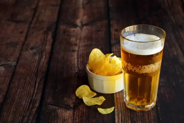 Light foamy beer with potato chips on a wooden table and have copy space.