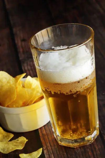 Light foamy beer with potato chips on a wooden table.