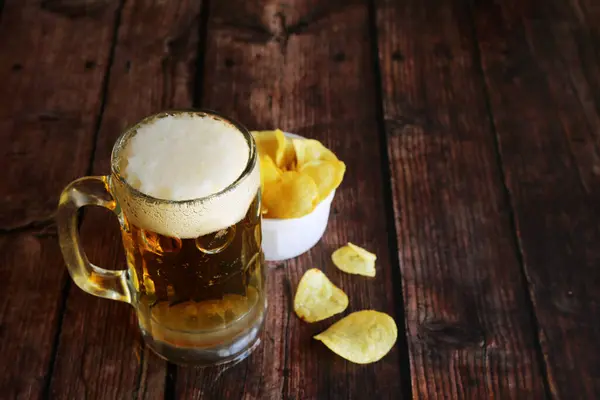 A mug of light foamy beer with potato chips on a wooden table and have copy space.