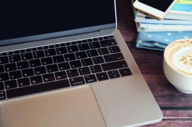 Laptop, bir fincan sıcak kahve, akıllı telefon ve dergi ile ahşap masada uzaktan kumandayla çalışıyor..