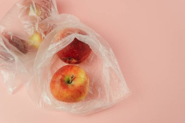 İçinde kırmızı elma olan plastik bir torba. Çanta pembe arka plana yerleştiriliyor. Elmayı tutmak için plastik poşet kullanıldığı için savurganlık ve çevresel endişe kavramı, ki bu doğal bir şeydir.