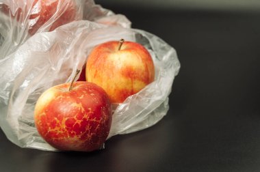 Siyah arka planda plastik bir çantada iki elma var. Elmalar kırmızı ve parlak.