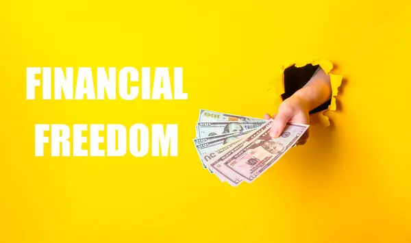 A hand holding a stack of money with the words financial freedom written below. Concept of financial independence and the importance of managing one\'s finances
