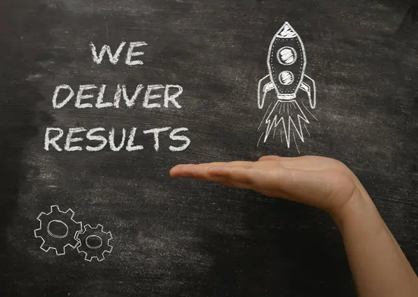 A hand holding a chalkboard with the words We deliver results written on it. The chalkboard also features a rocket, which symbolizes progress and achievement