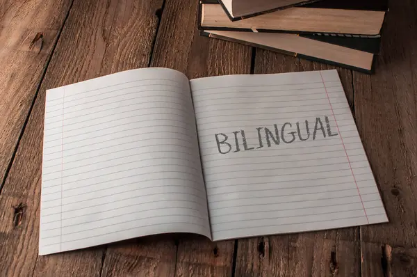 Bir defter üzerinde iki dilde yazılmış bir sayfa açar. Defter ahşap bir masanın üzerinde duruyor.