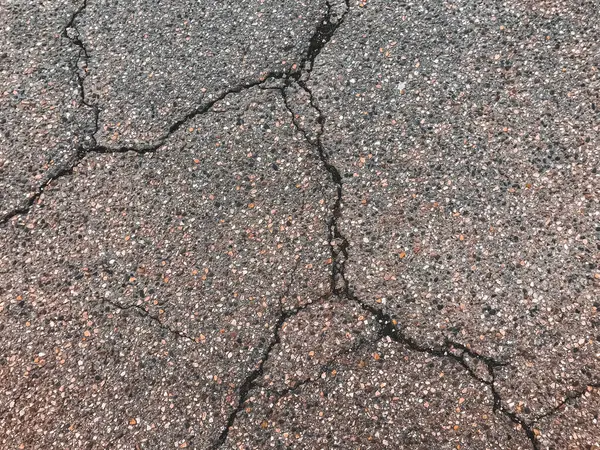 A cracked and broken road with a lot of gravel. The road is in a state of disrepair and is not safe for driving