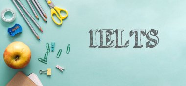 Bir sürü okul malzemesi ve elma olan yeşil bir arka plan. Arka planda IELTS kelimesi beyazla yazılır