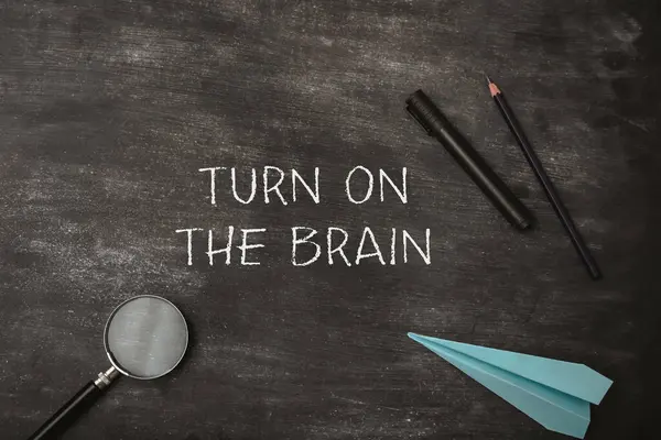 stock image Turn on the brain is written on the chalkboard. The chalkboard is covered with chalk and a pair of pencils. A blue paper airplane is also on the chalkboard