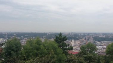 Bulutlu bir gökyüzü ve arka planda ağaçlar olan bir şehir manzarası. Şehir hareketli ve gökyüzü bulutlu.