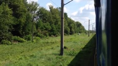 Arka planda ağaçlar olan bir tren raylarda ilerliyor. Tren otlarla çevrili bir raydadır.