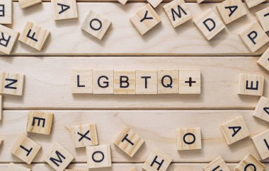 Ahşap harflerden oluşan bir karmaşa Lgbtq kelimesini heceliyor. Harfler ahşap yüzeye saçılmış, kaos ve kargaşa hissi yaratıyor. Resim bir kapsayıcılık iletisi iletir