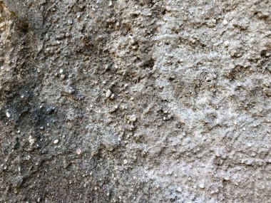 Üzerinde bir sürü toprak ve taş olan bir duvar. Duvar gri ve pürüzlü bir dokusu var.