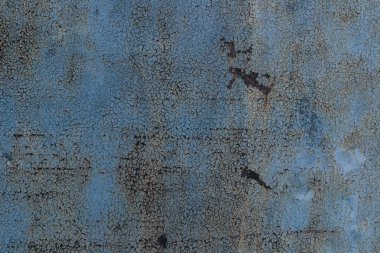 Bir sürü çatlağı ve deliği olan mavi ve paslı bir duvar. Duvar eski ve yıpranmış.