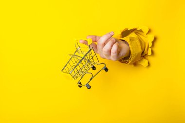 Sarı arka planda alışveriş arabasını tutan bir el. Mevsimlik alışveriş ve tanıtım konsepti