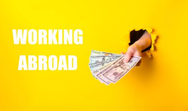 Altında yurtdışında çalışan kelimelerin yazılı olduğu bir yığın parayı tutan bir el. Ekonomik olarak bağımsız ve farklı ülkelerde çalışma yeteneğine sahip birinin düşüncesi