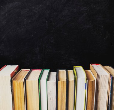Kara karatahtanın üzerinde bir sıra kitap. Kitaplar farklı boyutlarda ve renklerde. Kitaplar, soldaki en büyük ve sağdaki en küçük kitapla düzenli olarak düzenlenir.