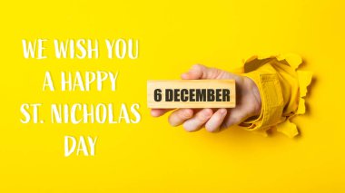 A person holding a block of wood with the words We wish you a happy 6th St. Nicholas Day written on a yellow background