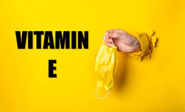 Altında E vitamini yazan sarı bir maskeyi tutan bir el. İhtiyat anlayışı ve birinin sağlığıyla ilgilenmesinin önemi